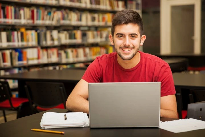 Top Travel & Tourism Courses illustrated by a smiling student studying on a laptop in a library with notebooks and books, symbolizing dedication to learning and a strong academic future in the tourism field.